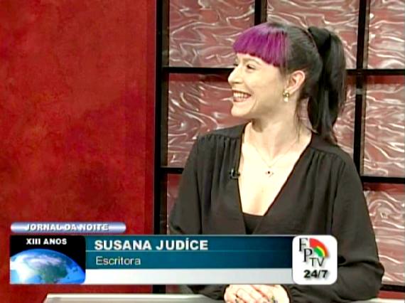 Mulher com cabelo preto e rosa num estúdio de televisão