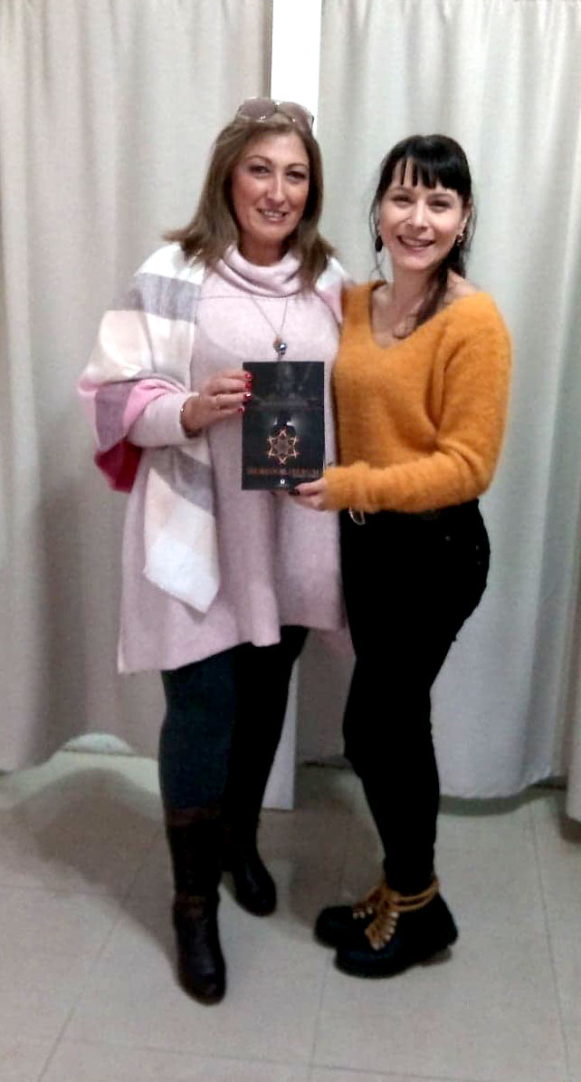 Duas mulheres num interior a segurar um livro preto com capa decorada em dourado e texto 'MINDSET ALEXANDER'.