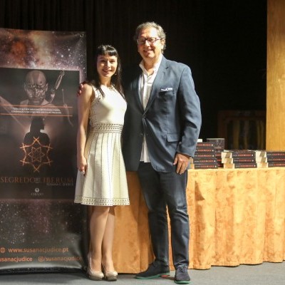 Cartaz e mesa com livros num evento com duas pessoas em pé ao lado