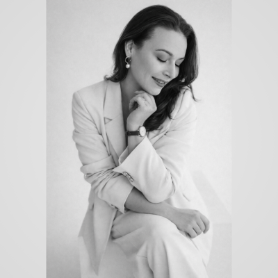 Mulher vestindo fato feminino claro e relógio de pulso, sentada e sorrindo em foto preto e branco