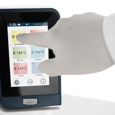 Ecrã tátil de dispositivo médico com interface colorida e mão enluvada a tocar.