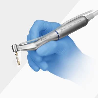 Peça de mão odontológica metálica com broca, segurada por mão com luva azul