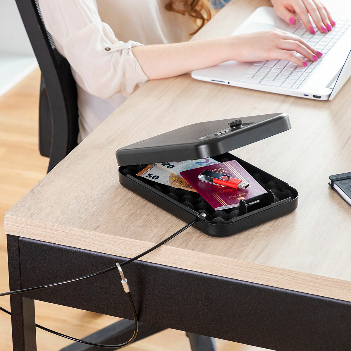 Cofre Portátil com Cabo de Segurança Prisaven InnovaGoods Caixa de segurança preta aberta sobre mesa com dinheiro e um cartão dentro, pessoa a usar computador ao fundo