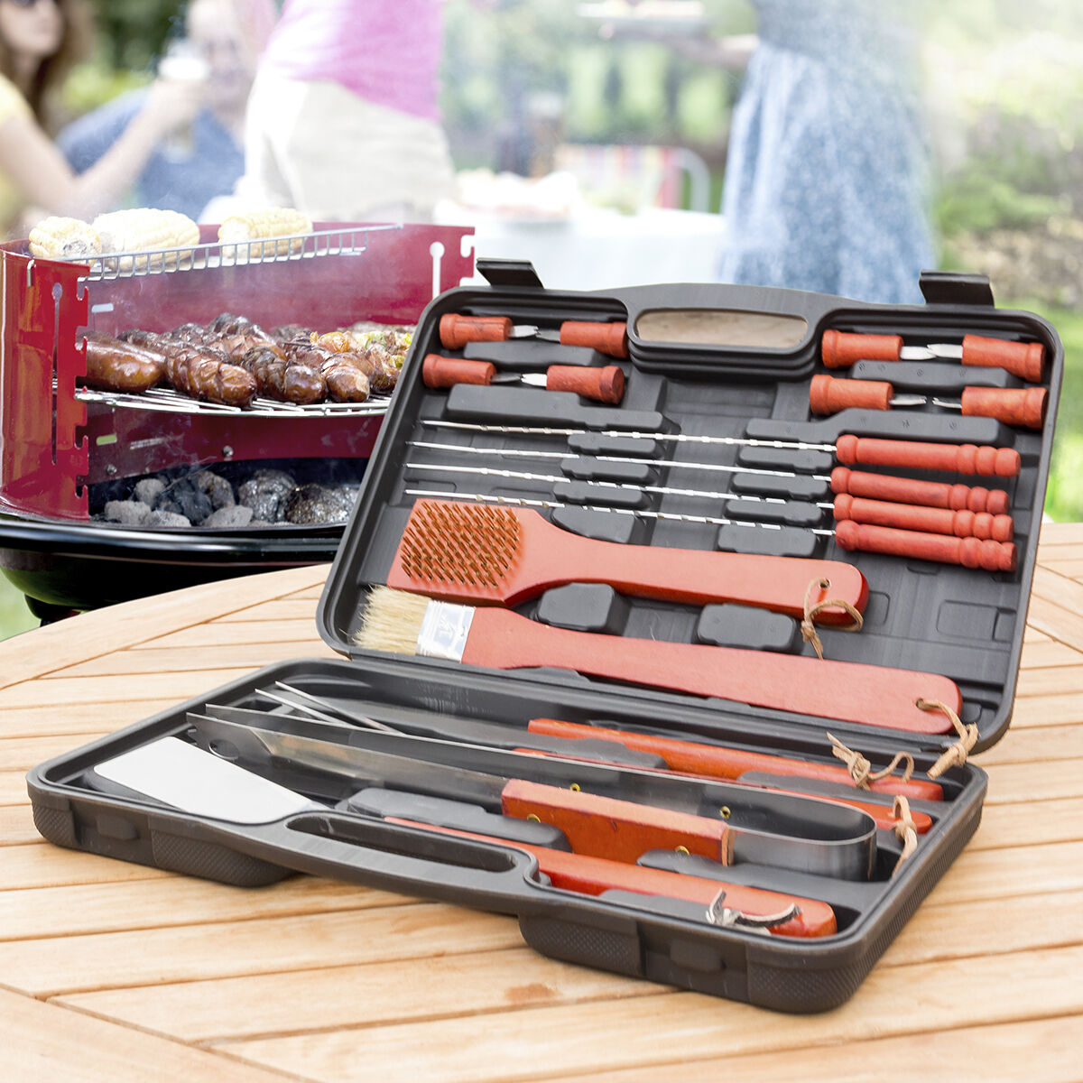 Maleta Grelhador Barbecase InnovaGoods 18 Peças Conjunto de utensílios para churrasco em estojo preto com cabos vermelhos sobre mesa de madeira ao ar livre