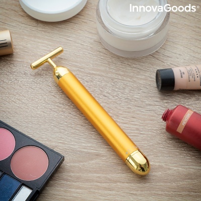 Dispositivo de beleza dourado entre produtos de maquilhagem sobre madeira clara