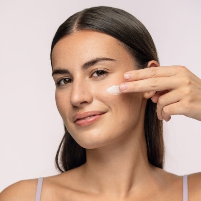 Mulher a aplicar creme no rosto com os dedos