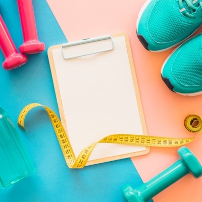 Equipamento de fitness incluindo halteres, sapatilhas, fita métrica, garrafa, relógio e prancheta sobre fundo colorido.