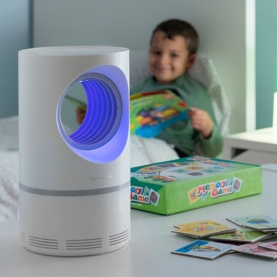 Dispositivo eletrónico branco com iluminação azul e jogo de tabuleiro Memory Game numa mesa, criança ao fundo numa cama.