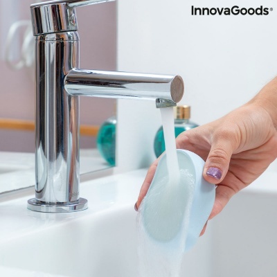 Tornea de lavar com mão segurando esponja azul translúcida sob água no lavatório branco