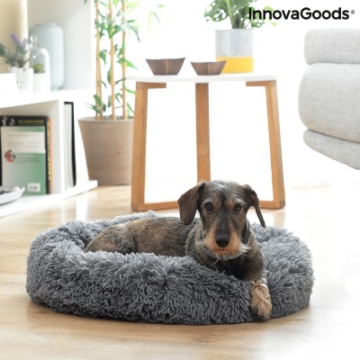 Cama redonda cinzenta para cães, com cão deitado, em sala com chão de madeira e mesa clara