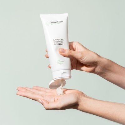 Bisnaga branca de creme para pernas cansadas sendo aplicada na palma da mão