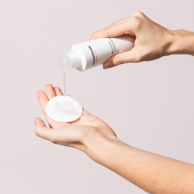 Frasco branco a verter líquido em disco de algodão em mãos femininas