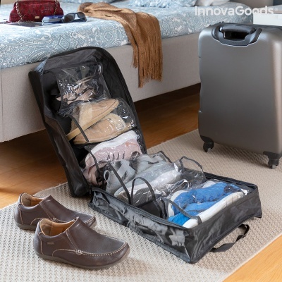 Necessaire organizadora de sapatos preta com compartimentos transparentes contendo sapatos, junto a sapatos castanhos e mala cinza ao lado da cama