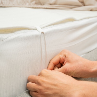 Capa de colchão branca a ser ajustada com elástico em colchão branco.