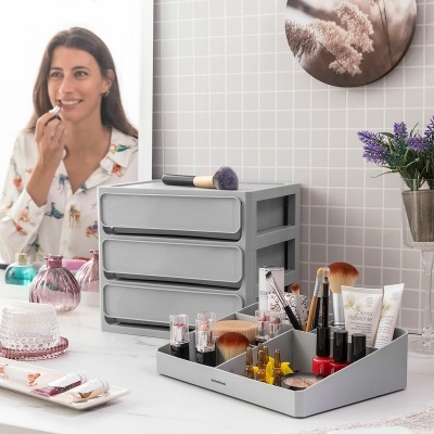 Organizador de maquilhagem cinza de plástico com vários cosméticos numa bancada branca