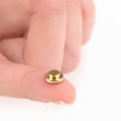 Botão metálico dourado redondo sendo segurado entre os dedos