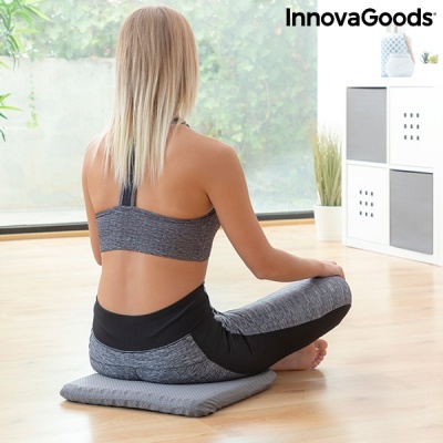 Mulher sentada com roupa desportiva cinzenta e preta numa almofada cinzenta no chão de madeira