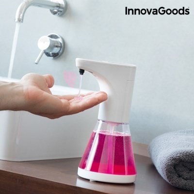 Dispenser automático de sabão líquido cor de rosa num lavabo com torneira e toalha cinzenta