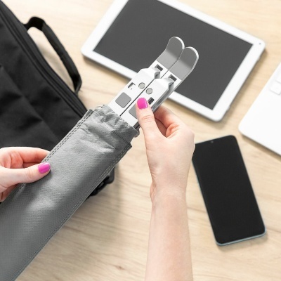Suporte ajustável metálico para tablet ou smartphone com capa cinza, mãos segurando, sobre mesa de madeira clara com dispositivos eletrónicos