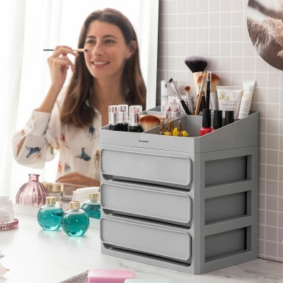 Organizador cinzento de maquilhagem com três gavetas cheio de produtos de beleza sobre uma bancada de banheiro