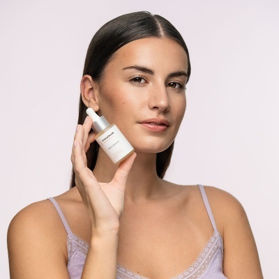 Mulher a segurar frasco branco com conta-gotas sobre fundo claro