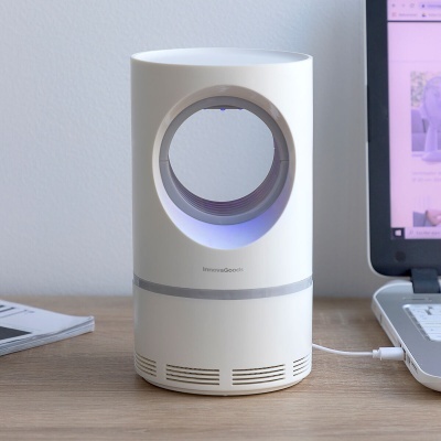 Aparelho electrónico branco cilíndrico com abertura circular e luz azul, sobre mesa junto a computador portátil