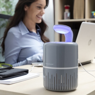 Humidificador cinzento com luz azul numa secretária junto a computador portátil e mulher a trabalhar