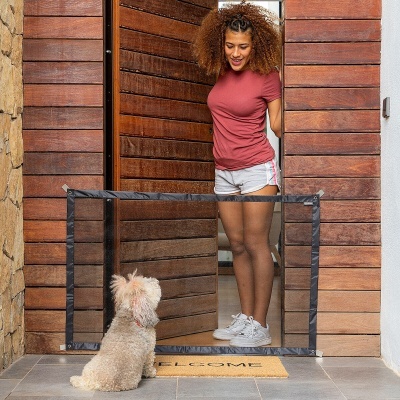 Mulher com roupa casual junto a porta de madeira com rede de proteção para animais e cão pequeno sentado no chão.