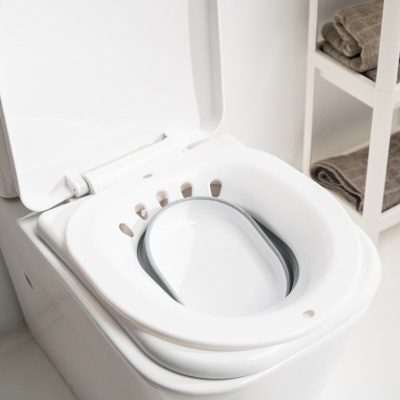 Assento sanitário branco com almofada de silicone cinzenta e prateleira com toalhas castanhas