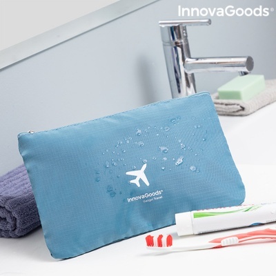Bolsa de viagem azul impermeável com fecho e logo InnovaGoods e avião branco numa casa de banho com escovas de dentes e toalhas.
