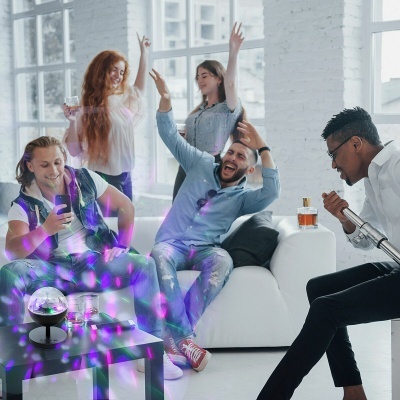 Grupo de jovens a festejar em sala moderna com luzes coloridas e garrafa de bebida