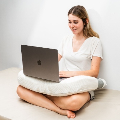 Mulher sentada com portátil Apple sobre almofada branca com textura acolchoada