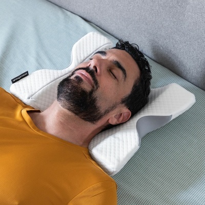 Travesseiro ergonómico branco com suporte para cabeça e pescoço numa cama