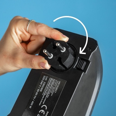 Dispositivo elétrico preto com ficha de dois pinos e botão deslizante em fundo azul