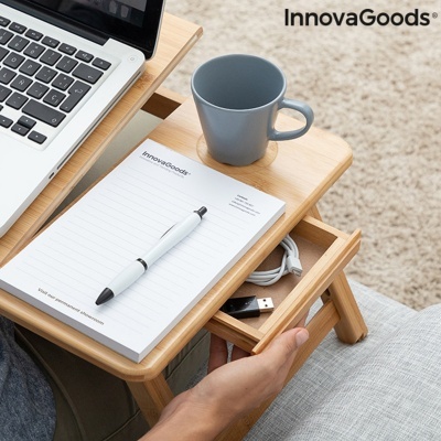Mesa portátil de madeira com gaveta aberta, bloco de notas InnovaGoods, caneta, chávena cinzenta e portátil cinzento