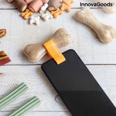 Suporte de telemóvel em forma de osso com etiqueta InnovaGoods ao lado de telemóvel e guloseimas caninas