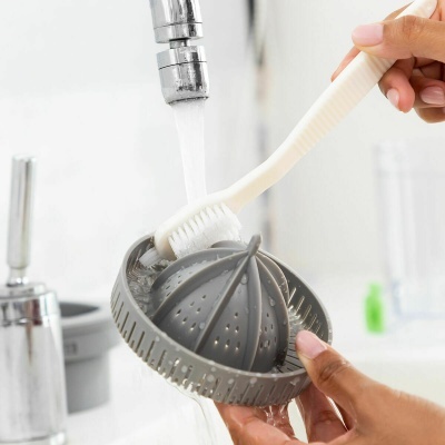 Pessoa a lavar espremer citrinos de plástico cinzento com escova de dentes branca sob torneira