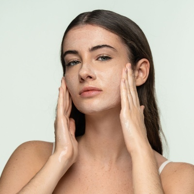 Mulher aplica óleo facial nas mãos e rosto com fundo claro