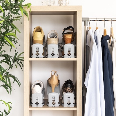 Sapatos organizados em estante de madeira clara com roupas penduradas e planta ao lado