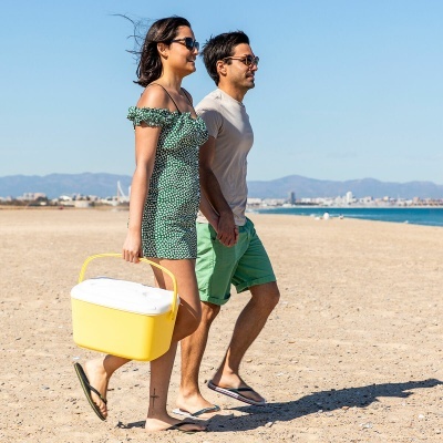 Casal caminhando na praia com caixa de plástico amarela e branca
