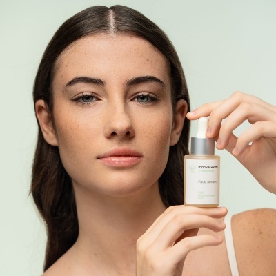 Mulher segura frasco de sérum facial InnovaGoods com fundo verde claro