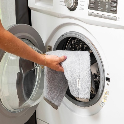 Máquina de lavar branca com porta redonda aberta e mão a colocar toalha cinza felpuda