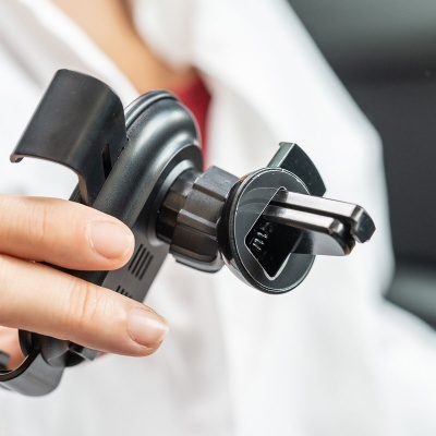 Suporte de telemóvel automóvel preto com clip para ventilação sendo segurado por uma mão