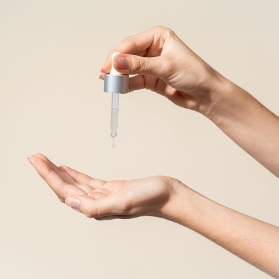 Mãos femininas a usar conta-gotas com líquido transparente sobre a palma da mão