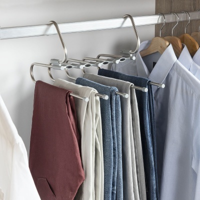 Cabides em metal e madeira com calças coloridas e camisas claras penduradas numa balda de metal