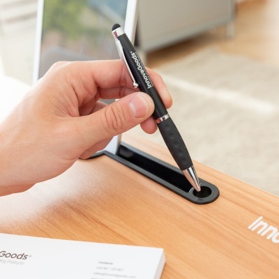 Caneta preta com punho emborrachado numa secretária de madeira clara com passagem para cabos.