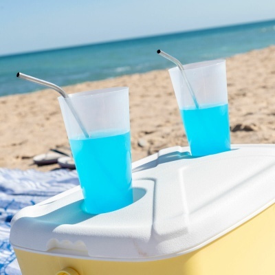 Dois copos com bebida azul e canudos em cooler amarelo na praia