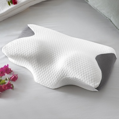 Almofada ergonómica branca e cinzenta com textura acolchoada numa cama branca e flores cor-de-rosa ao lado