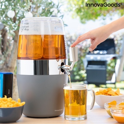 Dispenser de bebidas cinza com copo de vidro a ser cheio, perto de snacks numa mesa