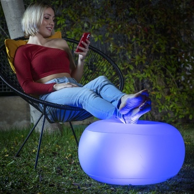 Mulher sentada em cadeira preta com pés em móvel iluminado azul no jardim à noite